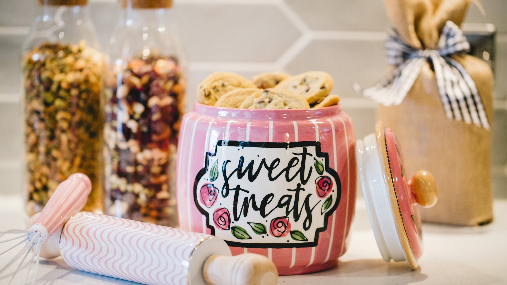 Hand painted pink cookie jar with 'sweet treats' text on a kitchen counter with jars and a rolling pin.