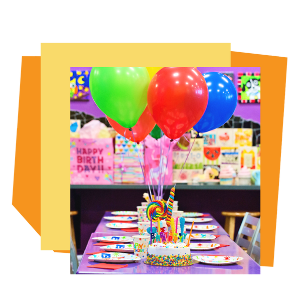 Colorful birthday table setup with balloons and cake in an As You Wish Pottery studio setting