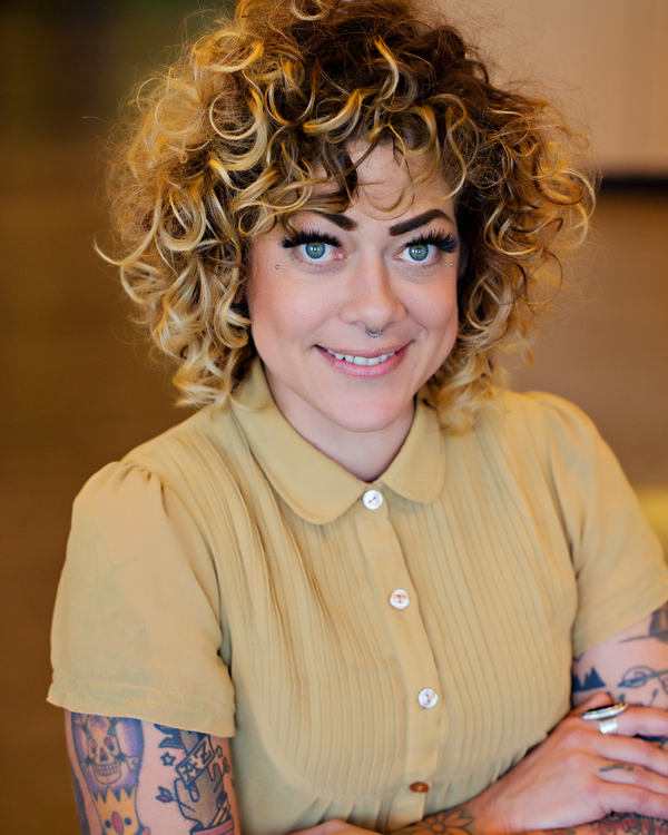 Person with curly hair wearing a yellow blouse with a blurred background