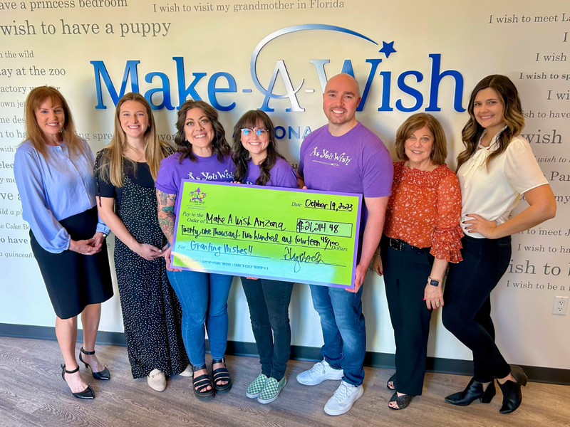 Group of people holding a large check in front of a Make-A-Wish sign.