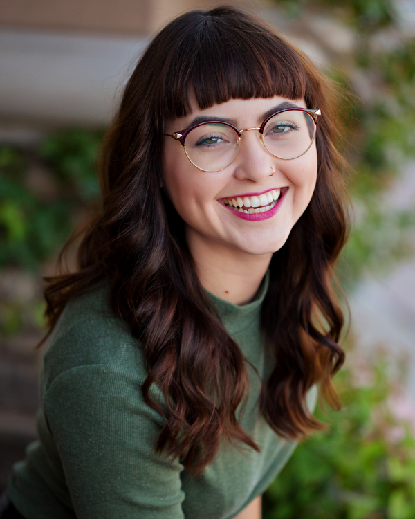Woman with glasses and a green sweater smiling outdoors